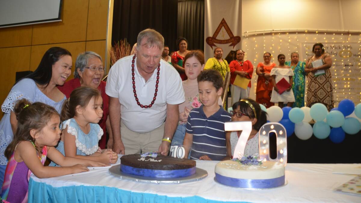 MAKE A WISH: Father Mick Lowcock gets some help to blow out the candles on his two 70th birthday cakes.