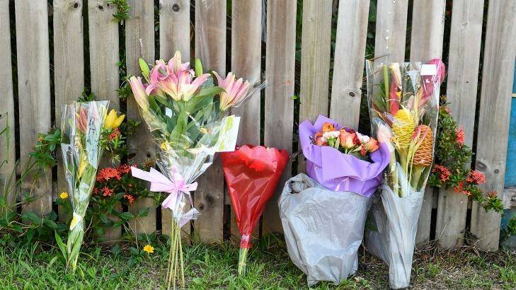 Flowers are seen laying up against a fence across the road from the scene of a multiple stabbing in the suburb of Manoora. Photo: Ian Hitchcock
