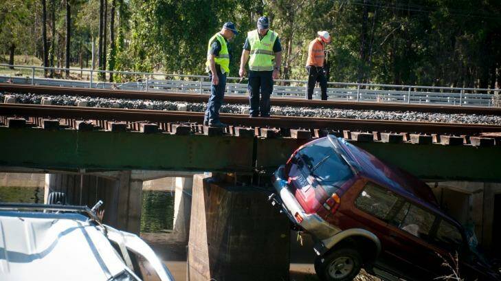 Police recover vehicles swept off a bridge by floodwaters. Photo: Robert Shakespeare