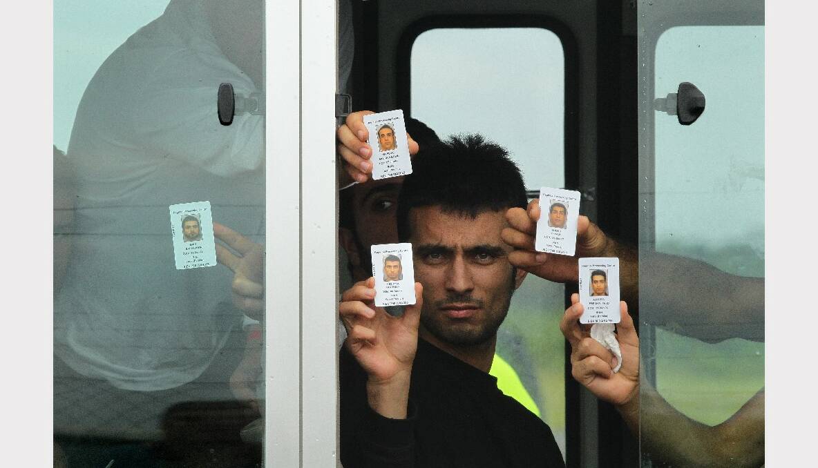 Pezhma Ghorbani 26 from Iran (center) along with his fellow asylum seekers holds his ID card at the window of the bus after arriving on the second plane carrying asylum seekers to Manus Island. Photo: Kate Geraghty 