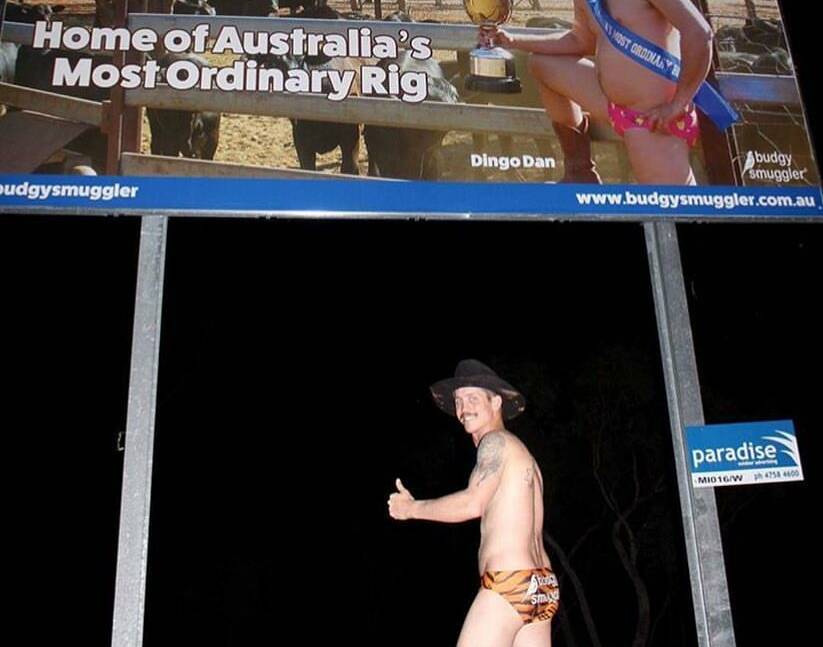 Stacie Campbell is the first to try to get a voucher for standing in front of the billboard in his budgie smugglers. 