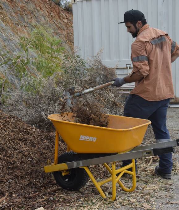 GRUNT WORK: A member of the Glencore scaling crew shovels wood chips in an effort to help beautify the Mount Isa Underground Hospital and Museum gardens. Photo: Danaella Wivell