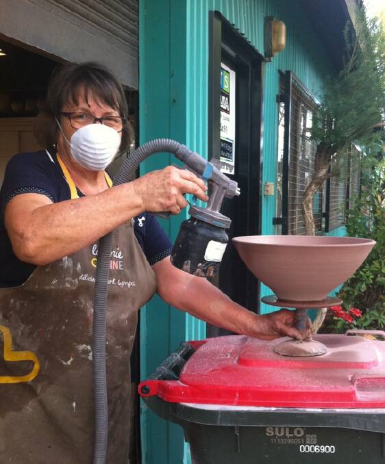 GLAZE ON: Savoye uses a spray gun to glaze one of her pottery bowls outside Arts on Alma, where she teaches classes and exhibits work.