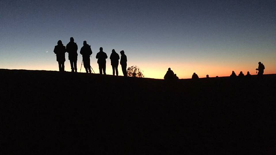 Early risers at the Big Red Bash climb the dune to catch the sunrise at the sand dune. Photo: Derek Barry
