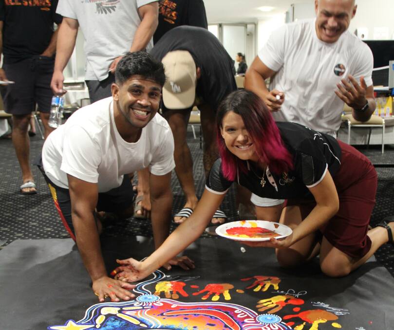 Chern'ee Sutton and players including Andrew Fitifa add handprints to the painting.